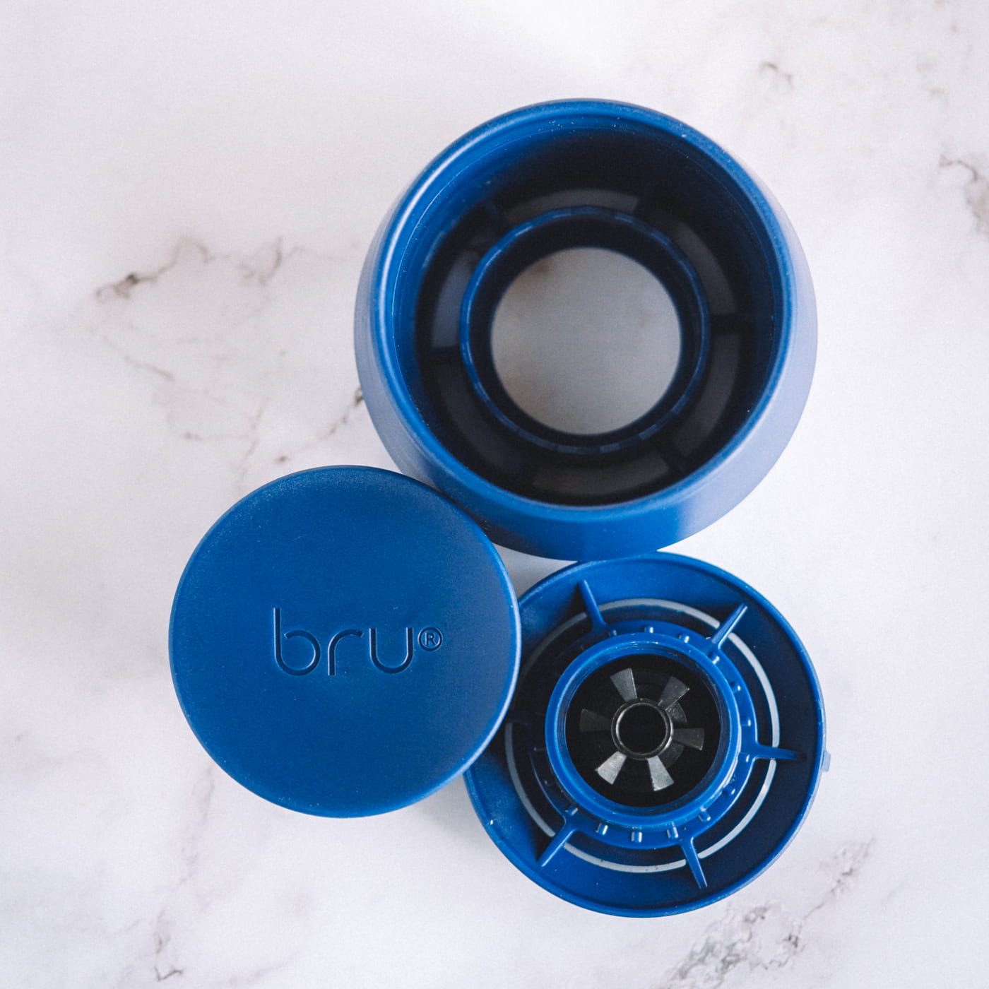 Easy cleaning block: Blue bru travel mug disassembled on a marble surface showing the lid and removable parts for easy cleaning